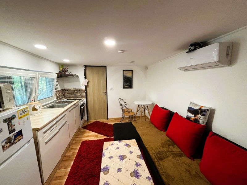 Celoročne obývateľná chata v Gabčíkove na 150 m² pozemku pri Dunaji - Interiér chaty s kuchyňou, červenými vankúšmi a podlahou s dreveným dekorom.