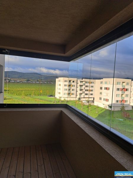 PREDAJ NADŠTANDARDNÉHO 4 IZB.BYTU V NOVOM KOMPLEXE-VINICE-150,18 m2 - Zasklený balkón ponúka výhľad na moderné budovy a zeleň, vhodný pre 4-izbový byt.