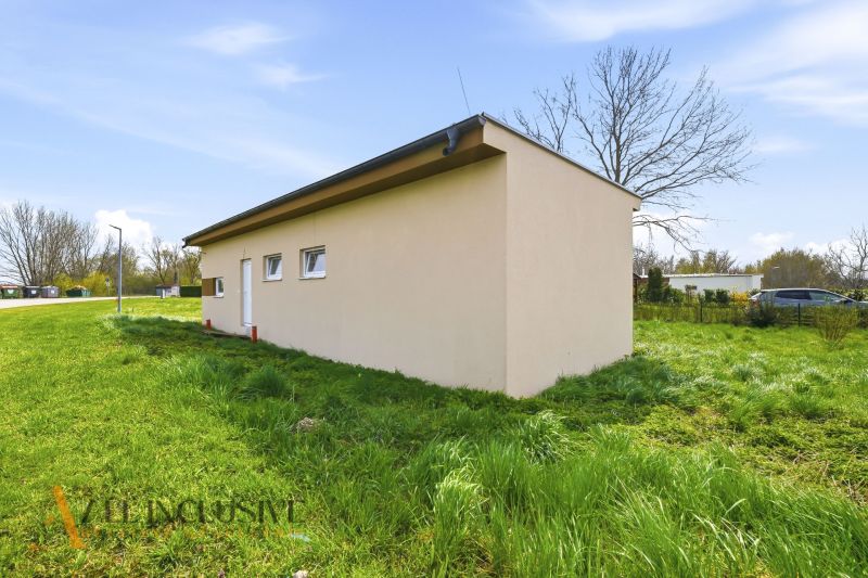 Na predaj rekreačný dom pri jazere, Vojka nad Dunajom - Chata vo Vojke nad Dunajom obklopená zeleňou, vedľa asfaltová cesta.