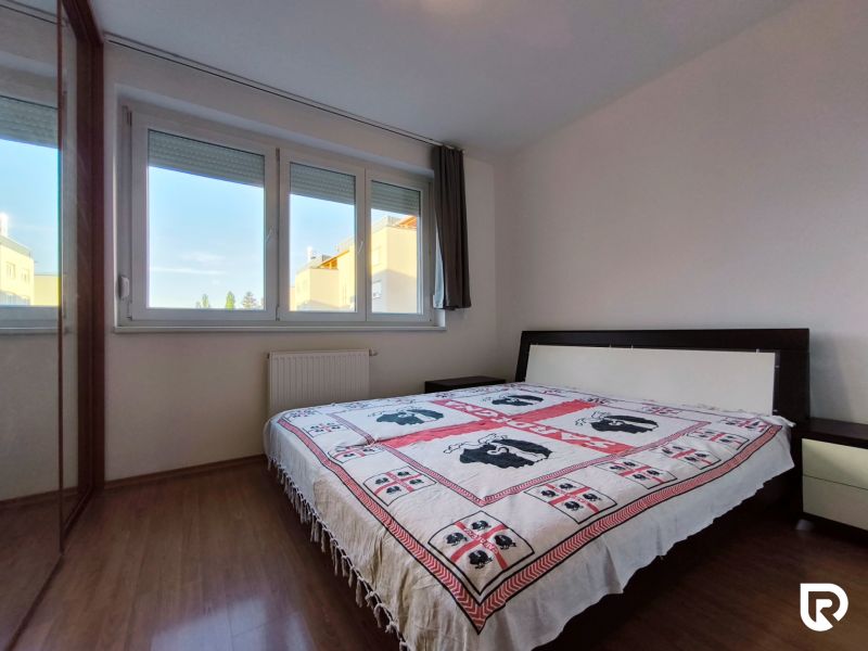 | priestranný | 2i byt s balkónom | parkovaním | Koprivnická - Spálňa v 2-izbovom byte s podlahou s dreveným dekorom a veľkým oknom.
