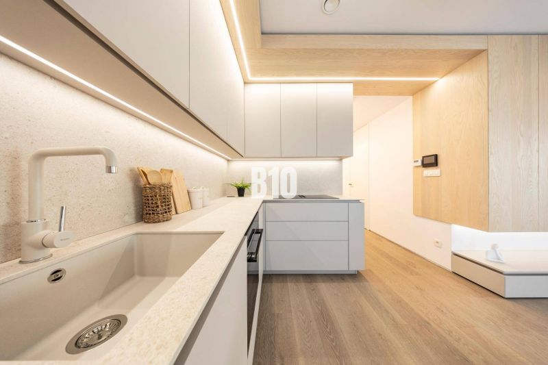 POD VINICAMI - 3IZBOVÉ BYTY V NADŠTANDARDNEJ BOUTIQUE REZIDENCII - Kuchyňa v 3-izbovom byte s podlahou s dreveným dekorom a minimalistickým dizajnom.