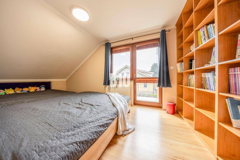 6-IZBOVÝ DOM S DVOJGARÁŽOU A VEĽKORYSÝM PRIESTOROM PRE CELÚ RODINU V P - Podkrovná izba s posteľou, knihovnicou a podlahou s dreveným dekorom v rodinnom dome.