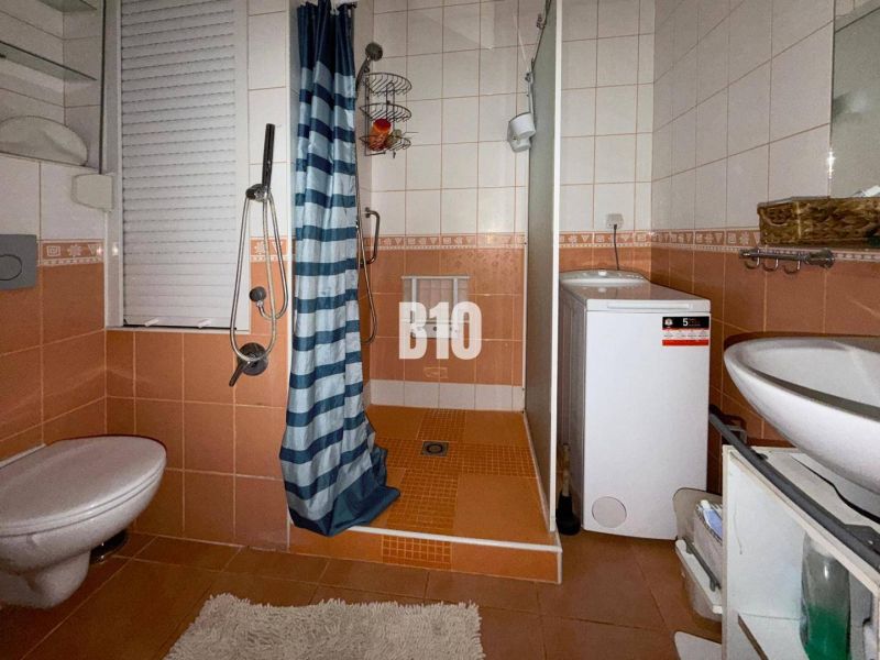 Perspektívny 3 izbový byt RUŽOMBEROK - Kúpeľňa v 3-izbovom byte s oranžovými obkladačkami, sprchovacím kútom, práčkou a WC.