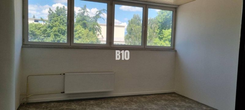 Prenájom obchodných a kancelárskych priestorov - Izba s veľkým oknom, bielymi stenami a podlahou s dreveným dekorom.