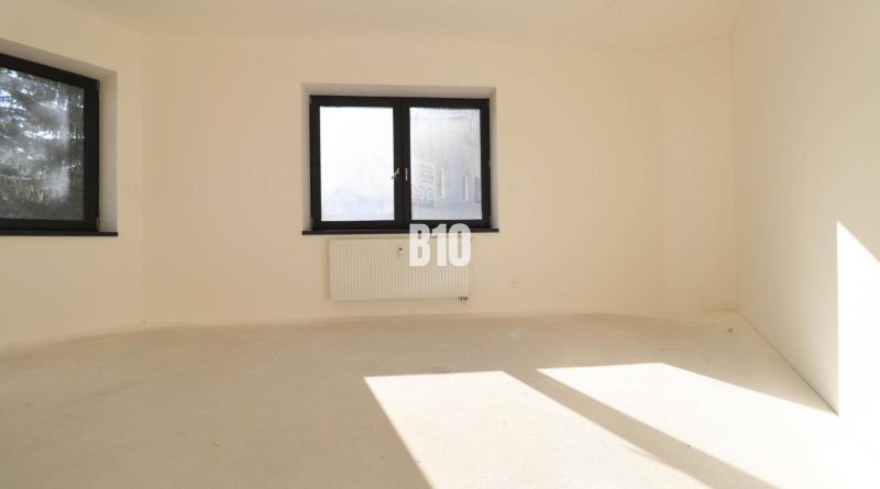 VÝNIMOČNÁ INVESTIČNÁ PRÍLEŽITOSŤ! ADMINISTRATÍVNY PRIESTOR (127,87 m²) - Prázdna kancelária s dvoma oknami a radiátorom, svetlé steny, podlaha bez dekoru dreva.