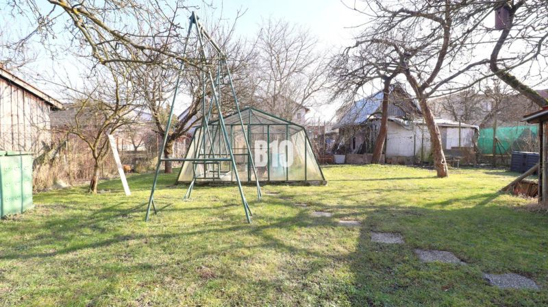 Veľký rodinný dom Turany - Záhrada rodinného domu v Turanoch s hojdačkou a skleníkom, obklopená stromami.