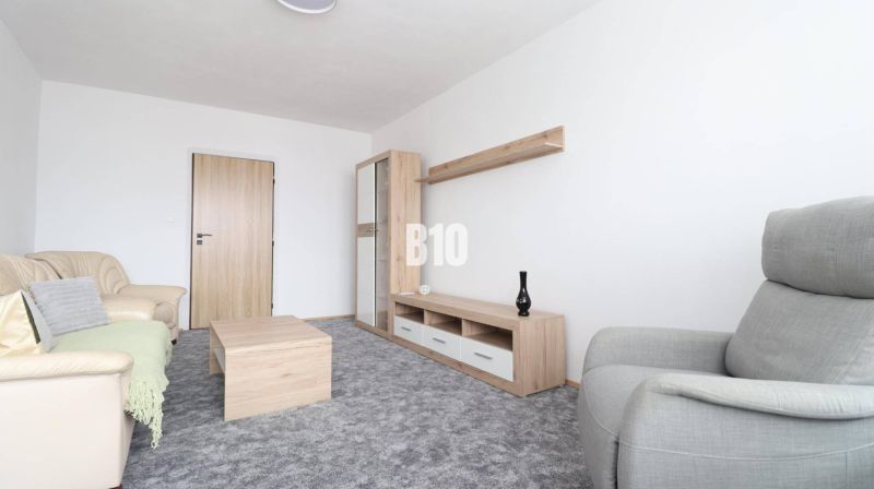 Na prenájom 3 izbový veľkometrážny byt Nováková ulica - Obývacia izba s béžovou sedačkou, šedým kreslom a nábytkom s dreveným dekorom v 3-izbovom byte.