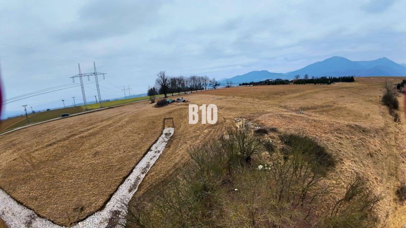 Veľký stavebný pozemok na predaj - Laskár - Kopcovitá krajina v Laskári vhodná pre pozemky na bývanie, s elektrickým vedením v pozadí.