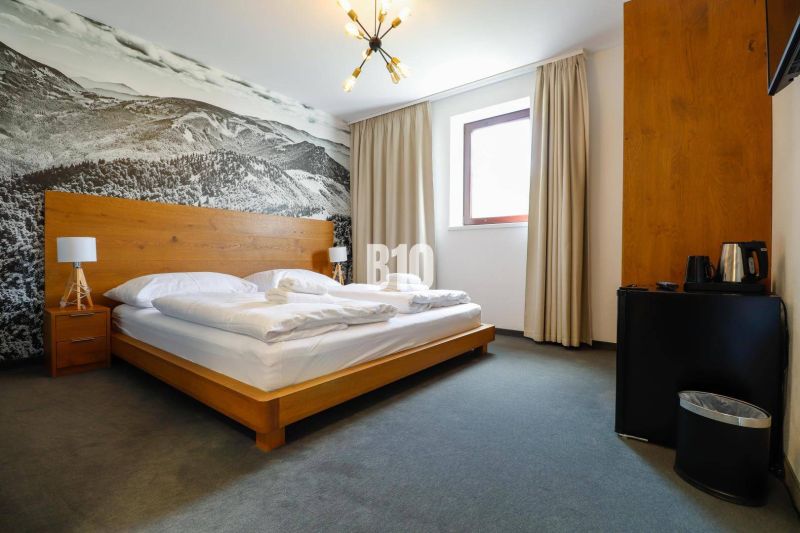 VKUSNE ZARIADENÝ apartmán v TOP lokalite v lyž. stredisku SNOWLAND Val - Spálňa v rekreačnom apartmáne s drevenou posteľou a veľkoformátovou fotografiou krajiny.