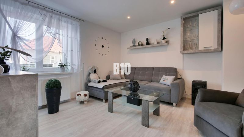 Ideálne bývanie: Zariadený dom 85m² s nízkymi nákladmi - Obývacia izba v rodinnom dome s podlahou s dreveným dekorom a šedým sedacím súpravou.