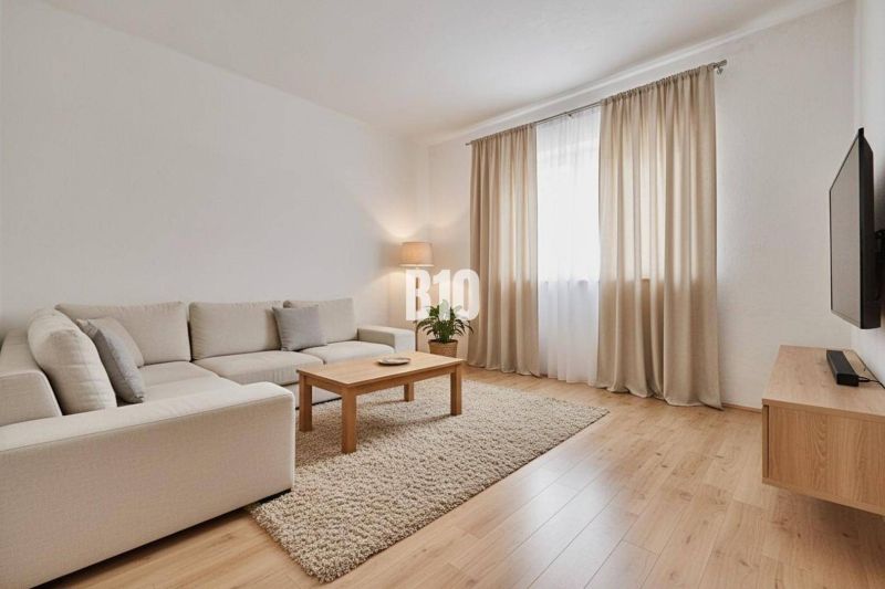 Rodinný dom s rovinatým 10a pozemkom - Obývacia izba rodinného domu s béžovou sedačkou, stolíkom a podlahou s dreveným dekorom.