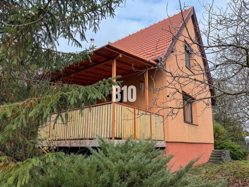 Priestranný rodinný dom s garážou na veľkom pozemku v obci Vlkas - Rodinný dom vo Vlkase obklopený zeleňou, tradične šikmá strecha, drevený balkón.