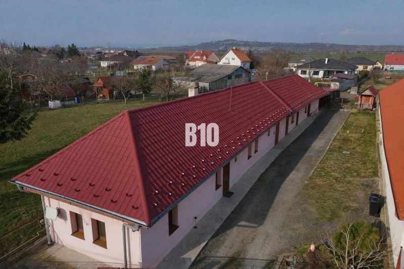 Rodinný dom s dvoma samostatnými bytovými jednotkami – Starý Hrádok - Rodinný dom v Leviciach s dlhým červeným strešným plášťom, obklopený záhradami.