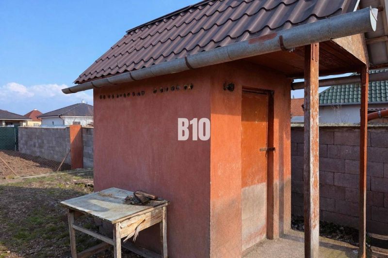 Rodinný dom s dvoma samostatnými bytovými jednotkami – Starý Hrádok - Malá murovaná stavba pri rodinnom dome v Leviciach, s plechovou strechou a dreveným stolom.