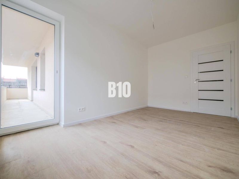 Novostavba -3 izbový byt neďaleko Trenčína - Izba s podlahou s dreveným dekorom a veľkými dverami na balkón v 3-izbovom byte.