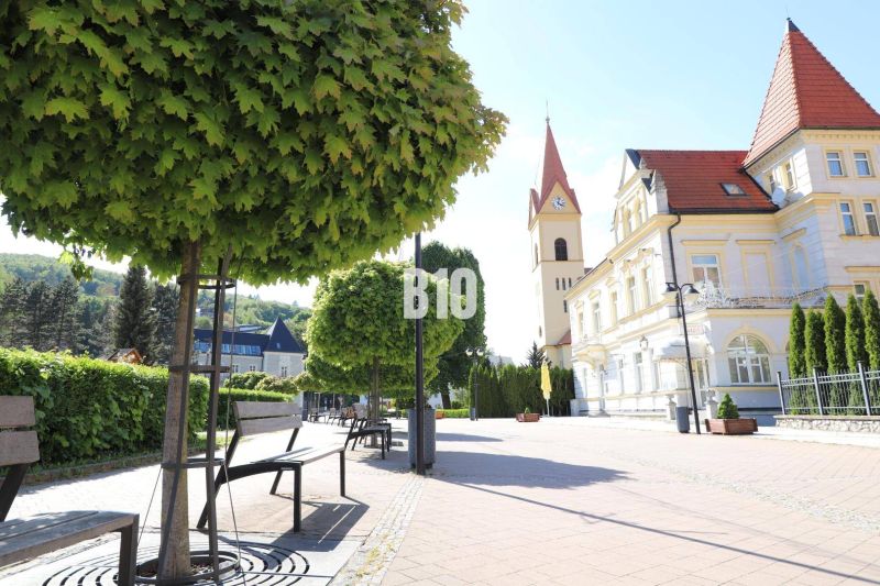 NOVÉ TEPLICE - stavebné pozemky v TOP lokalite - širšie centrum mesta  - Chodník s lavičkami a historická budova v Trenčianskych Tepliciach, pozemky - bývanie.