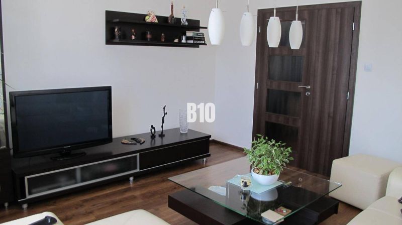 Priestranný 4 izbový byt - Solinky - Obývačka s televízorom, poličkami, stolíkom a podlahou s dreveným dekorom v 4-izbovom byte.