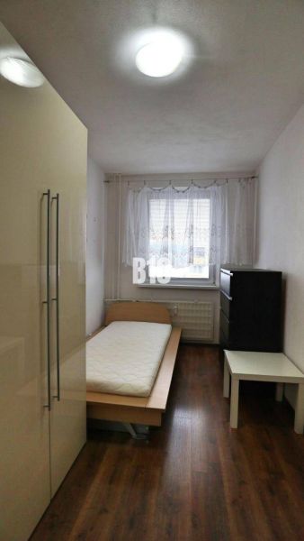Priestranný 4 izbový byt - Solinky - Jednoducho zariadená izba s jedným lôžkom a podlahou s dreveným dekorom v 4-izbovom byte.