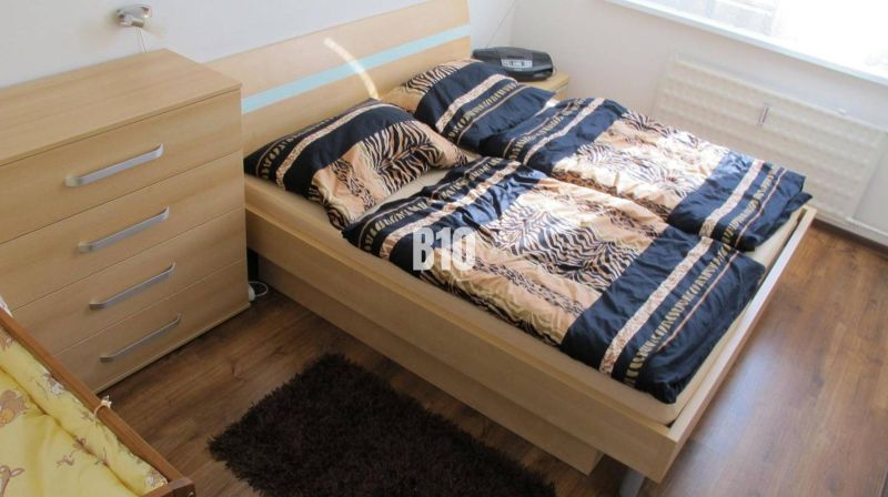 Priestranný 4 izbový byt - Solinky - Spálňa so vzorovaným posteľným prádlom, komodou a podlahou s dreveným dekorom v 4-izbovom byte.
