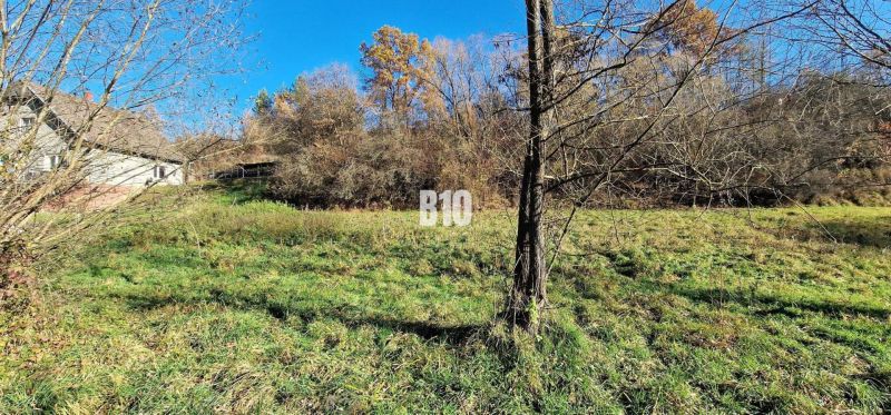 Rozľahlý, slnečný pozemok 2777m2 - Bytča - Rozľahlé pozemky na bývanie v Bytči, obklopené stromami s nehnuteľnosťou v pozadí.