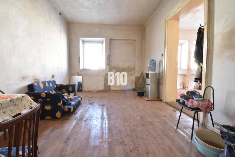 Rodinný dom na rekonštrukciu, 660m2 pozemok. - Obývacia izba v rodinnom dome s podlahou s dreveným dekorom, starší nábytok.