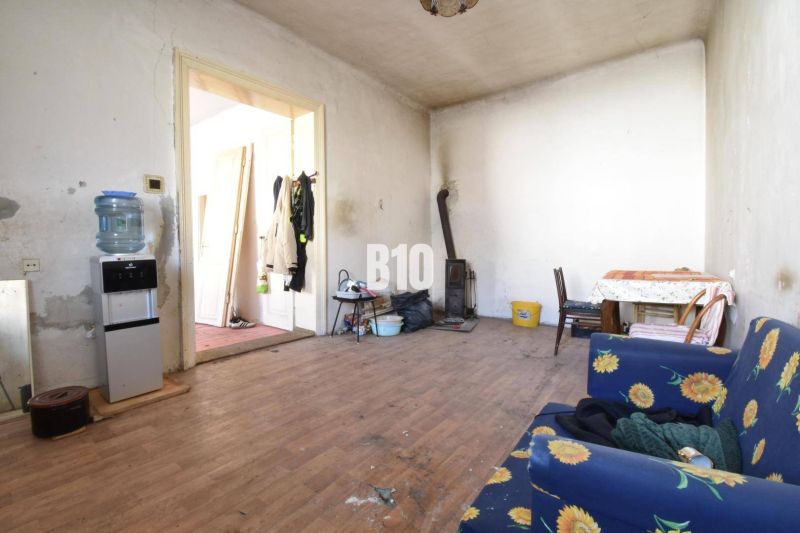 Rodinný dom na rekonštrukciu, 660m2 pozemok. - Izba v rodinnom dome s podlahou s dreveným dekorom, pec a nábytok s látkou s kvetmi.