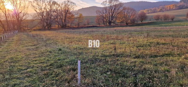 Slnečný pozemok s krásnym výhľadom, 1375m2. - Západ slnka nad zelenými poľami obklopenými stromami a vrchmi, ideálne pre pozemky - bývanie.