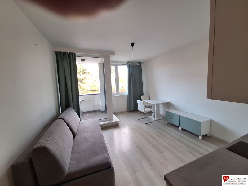 Ponúka na prenájom garsónku v komplexe Čerešne, Polianky Bratis - Garsónka s podlahou s dreveným dekorom, pohovkou, stolom a vstupom na balkón.