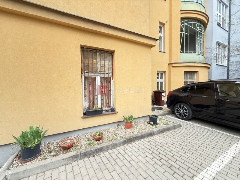 VEĽKORYSÝ 2i byt s rozlohou 76 m² v atraktívnej lokalite- Staré mesto - Parkovanie pred budovou na Leškovej v Bratislave s kvetináčmi a zaparkovaným autom.