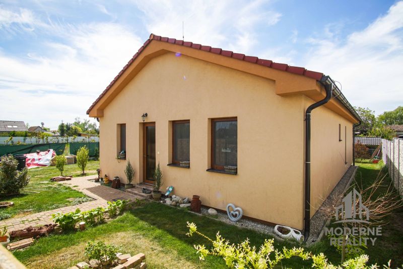 4-izbová novostavba rodinného domu s terasou, Andovce - Rodinný dom v Andovciach s upravenou záhradou, žltou fasádou a šikmou strechou.