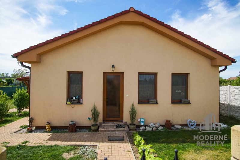 4-izbová novostavba rodinného domu s terasou, Andovce - Rodinný dom v Andovciach s tromi oknami, dvorom a kvetinovým záhonom.