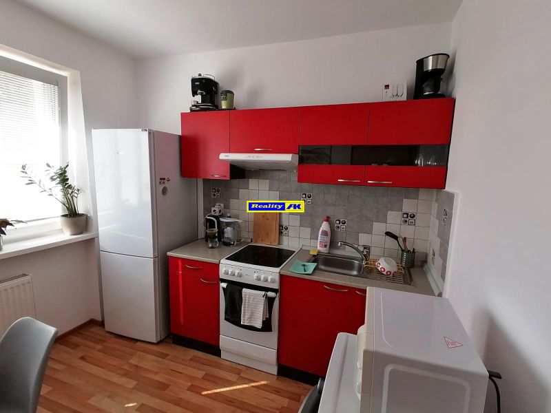1 izbový byt na predaj rekonštrukcia, Martin centrum, nový balkón - Kuchyňa s červenými skrinkami a podlahou s dreveným dekorom v 1-izbovom byte.