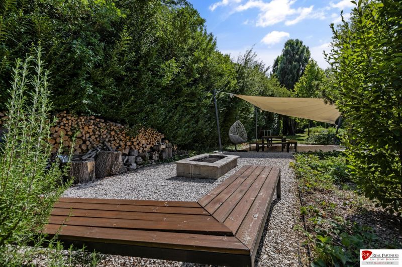 Na predaj nádherný 4 izbový luxusný byt,176 m2 + terasy 55 m2,2 garáž. - Záhrada s drevenou lavicou, krbom a tieniacou plachtou pri 4-izbovom byte na Rekreačnej v Piešťanoch.