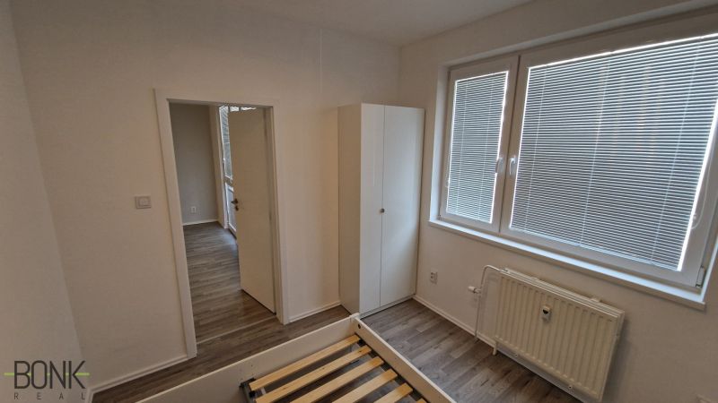 Predaj útulný, úplne prerobený 2 izbový byt s loggiou, Rajecká ulica. - Spálňa v 2-izbovom byte s bielymi stenami a podlahou s dreveným dekorom.