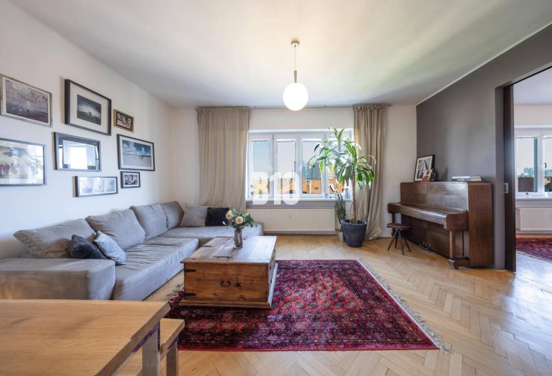 Prenájom | 2-izbový byt | Záhradnícka – Poľská ulica | 900 € + 200 € e - Obývačka s rohovou sedačkou, kobercom, klavírom a podlahou s dreveným dekorom.