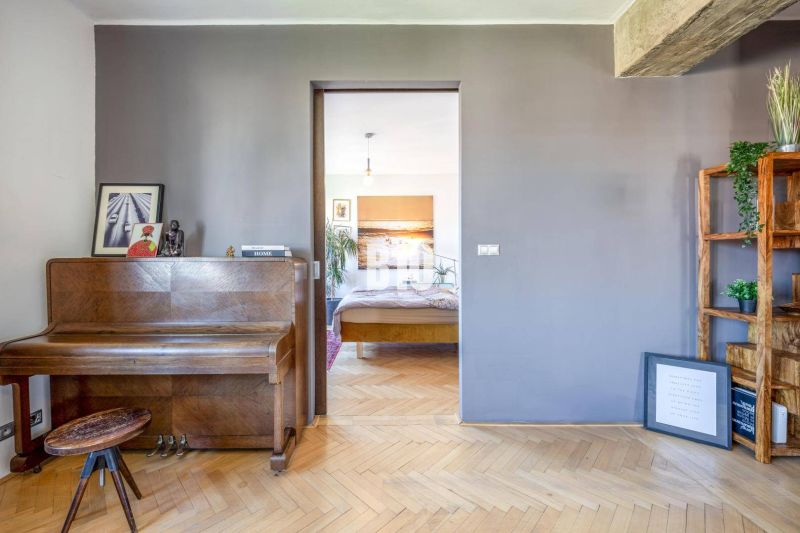 Prenájom | 2-izbový byt | Záhradnícka – Poľská ulica | 900 € + 200 € e - Interiér 2-izbového bytu s klavírom, kvetmi a podlahou s dreveným dekorom.