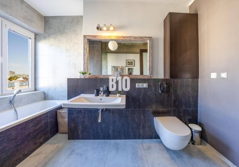 Prenájom | 2-izbový byt | Záhradnícka – Poľská ulica | 900 € + 200 € e - Kúpeľňa v 2-izbovom byte s vaňou, umývadlom, zrkadlom, výhľadom z okna a tmavými obkladmi.