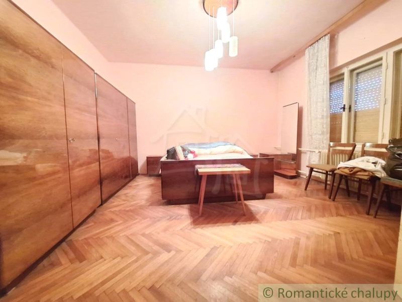 Priestranný pôvodný dom na rozľahlom pozemku v centre obce Gbelce - Spálňa v rodinnom dome s podlahou s dreveným dekorom, luster, skrine, stoličky.