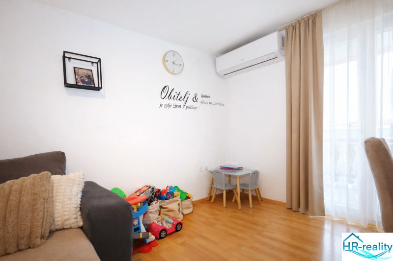 Vodice(HR)-Kompletne zariadený 3 izbový apartmán - Interiér Rekreačného apartmánu s hračkami, pohovkou a podlahou s dreveným dekorom.