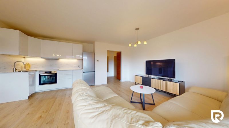 | Pekný a priestranný 3-izbový byt | 70m² |  - Obývacia izba s podlahou s dreveným dekorom, kuchyňou, sedačkou a televízorom v 3-izbovom byte.