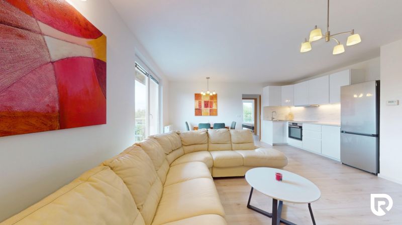 | Pekný a priestranný 3-izbový byt | 70m² |  - Svetlá obývačka s koženou sedačkou, kuchynským kútom a podlahou s dreveným dekorom v 3-izbovom byte.