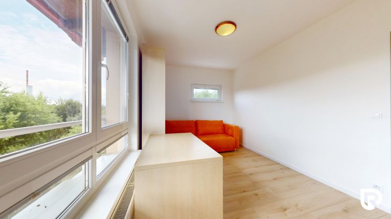 | Pekný a priestranný 3-izbový byt | 70m² |  - Izba s oranžovou sedačkou, veľkým oknom a podlahou s dreveným dekorom v 3-izbovom byte.