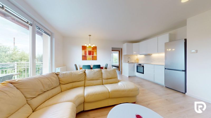 | Pekný a priestranný 3-izbový byt | 70m² |  - Obývacia izba 3-izbového bytu s podlahou s dreveným dekorom, kuchyňou a balkónom.