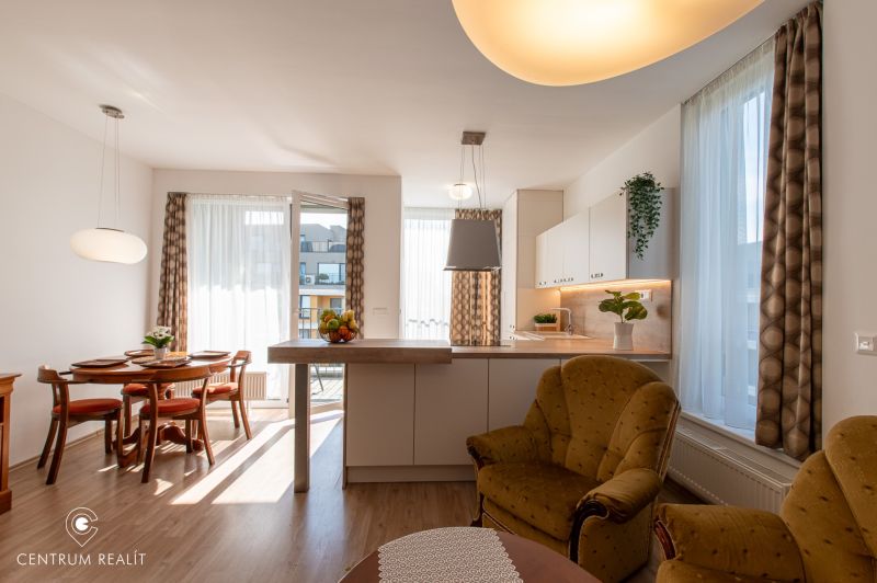 Moderný 2-izbový apartmán s parkovaním, Vila Leonardo, Bajkalská - Obývačka spojená s kuchyňou, jedálenský stôl, podlaha s dreveným dekorom, svetlé závesy.