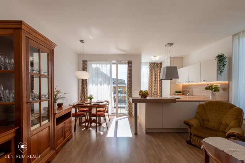 Moderný 2-izbový apartmán s parkovaním, Vila Leonardo, Bajkalská - Obývacia izba s kuchyňou v 2-izbovom byte, podlaha s dreveným dekorom, jedálenský stôl.