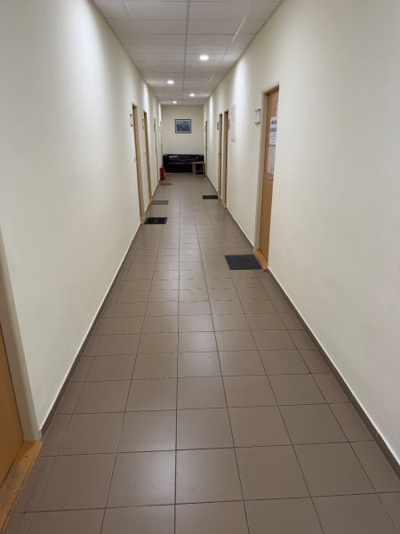 Ponúkame najlacnejšie  kancelárske priestory v Prievidzi  - Úzka chodba v kanceláriách s dlažbou, dverami a pohovkou na konci.