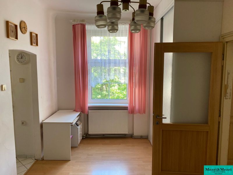 Byt na rekonštrukciu v centre Bratislavy – výborný projekt - Izba s podlahou s dreveným dekorom a ružovými závesmi v 2-izbovom byte.