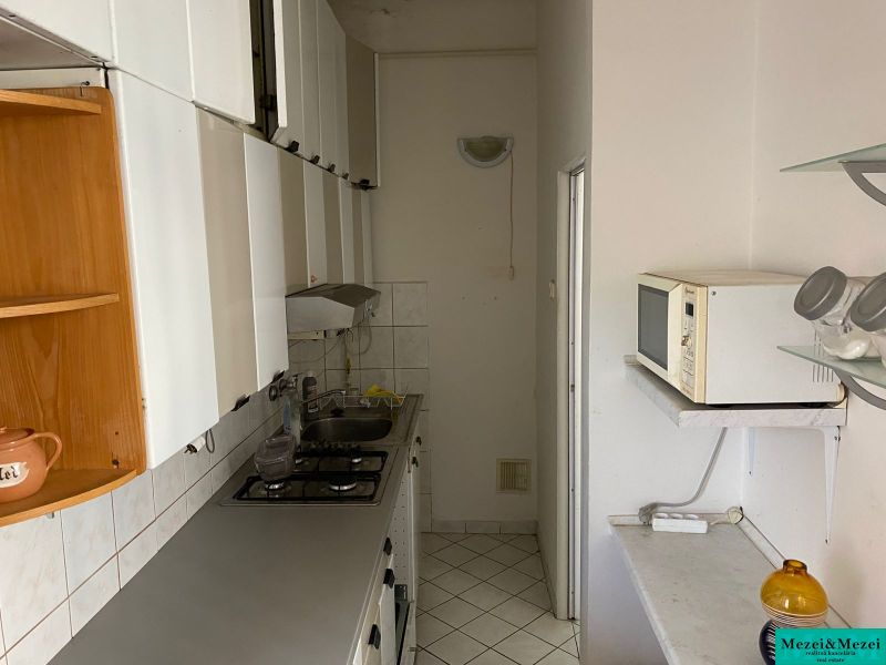 Byt na rekonštrukciu v centre Bratislavy – výborný projekt - Úzka kuchyňa v 2-izbovom byte s bielym nábytkom a kachličkami.