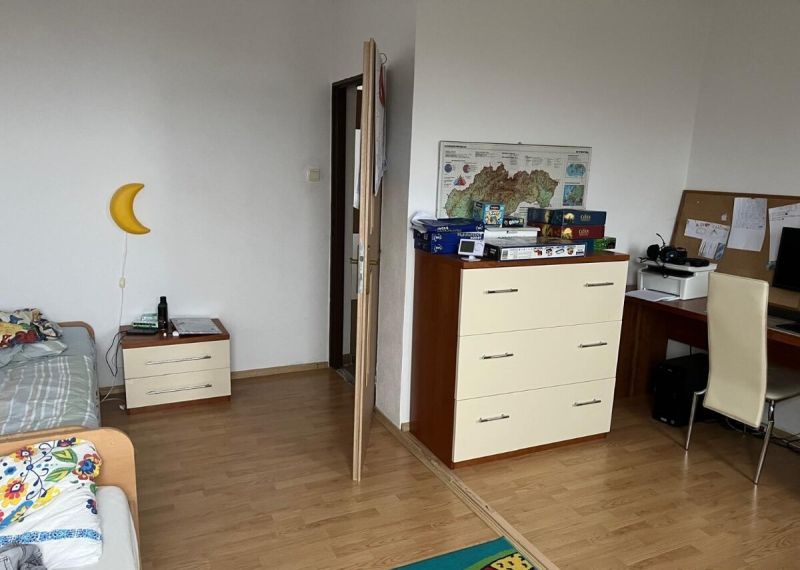 Rodinný dom v Štitároch s výhľadom a pod lesom - Izba v rodinnom dome s posteľou, komodou, stolom a podlahou s dreveným dekorom.