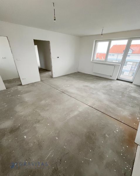 Na predaj 3 izb. byt s balkónom blízko centra - Izba v 3-izbovom byte, biele steny, veľké okno a surová podlaha.